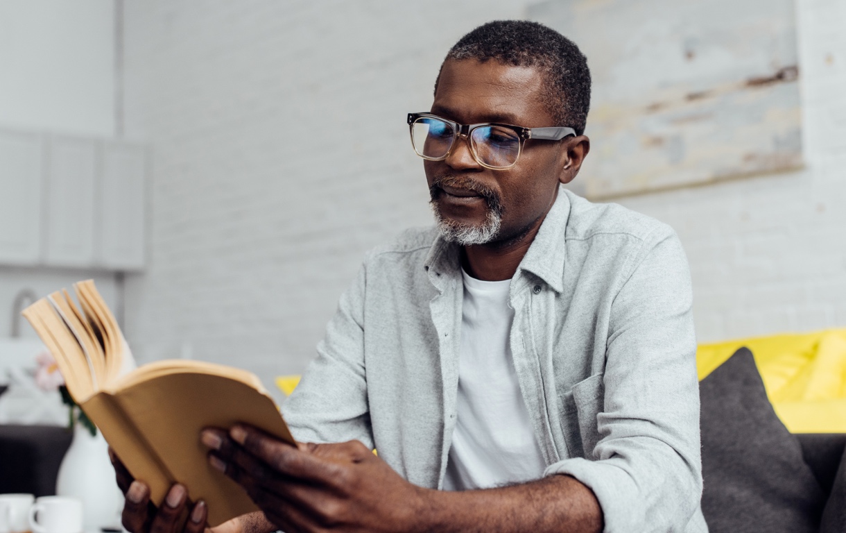 Older African American man with glasses reading book
